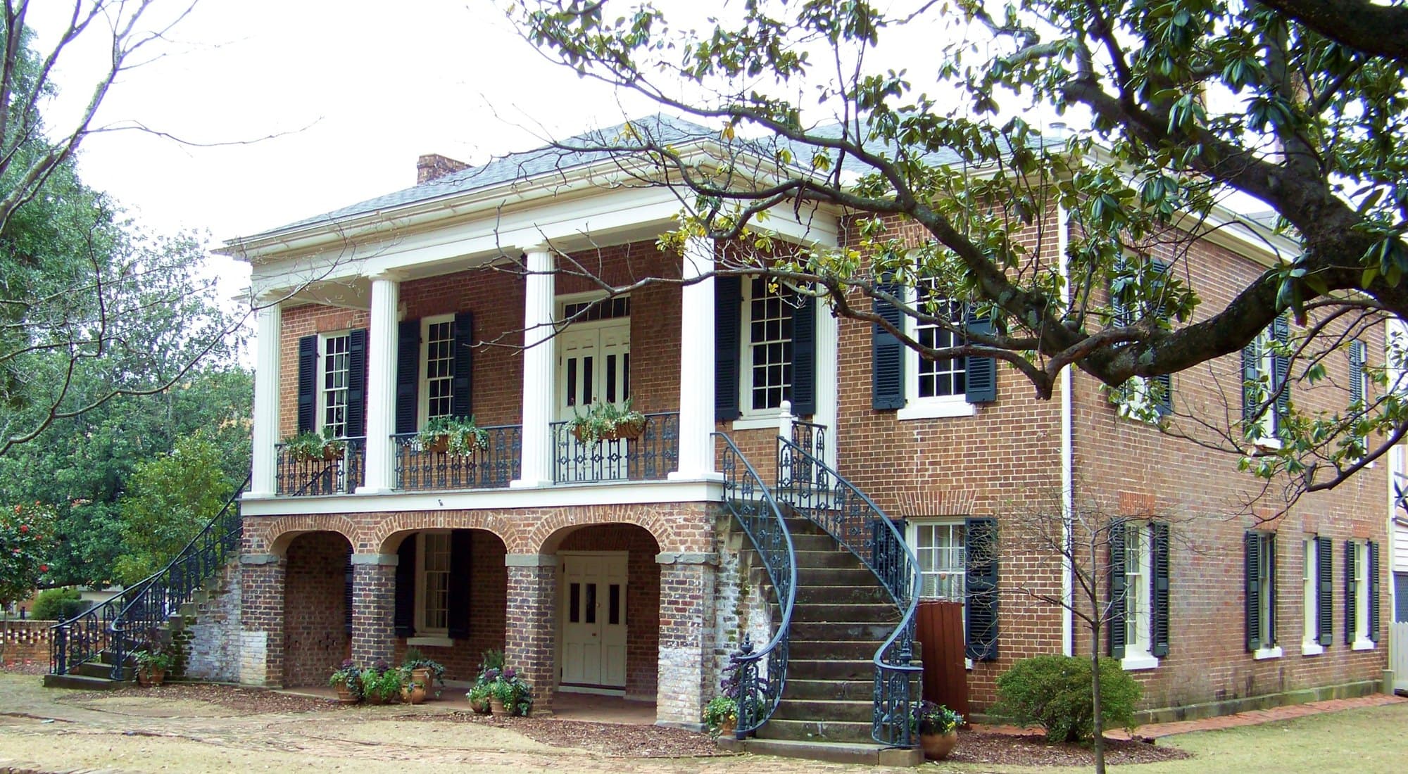 The Gorgas House Museum, a two-story Federal-style brick building on the University of Alabama campus, with white columns, a wrought-iron balcony and curved twin staircases rising to the main entrance